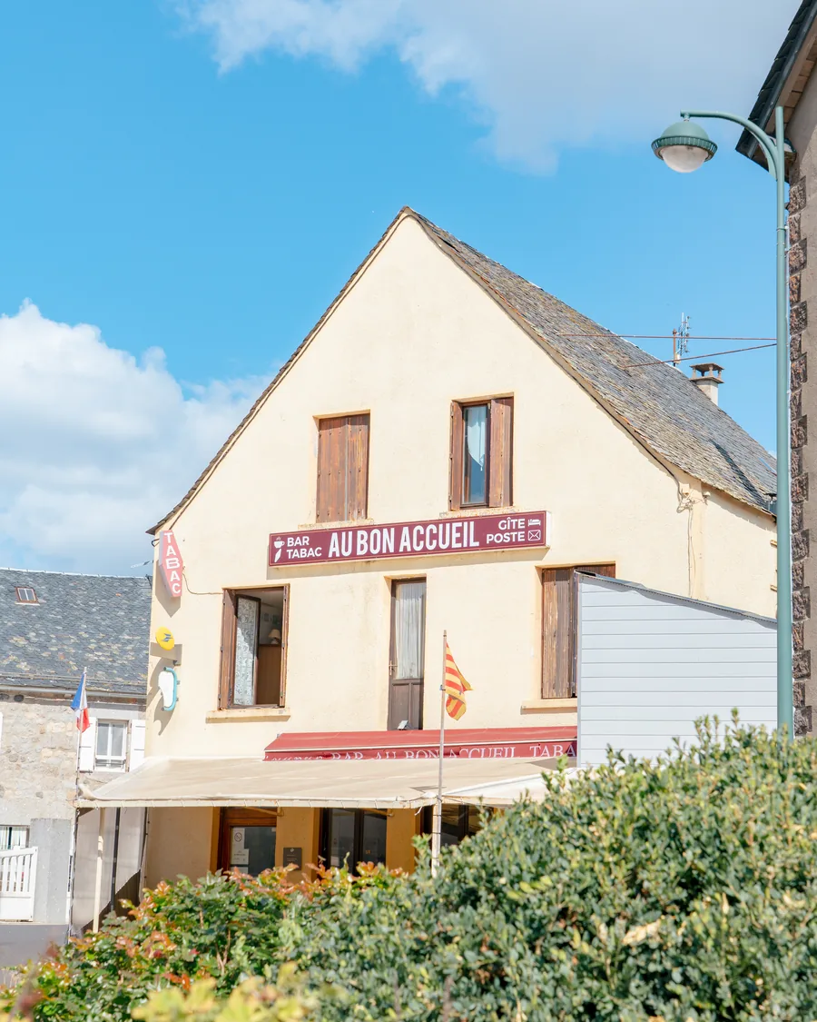 La façade d'Au Bon Accueil à Malbouzon : l'enseigne rouge annonce le bar, le tabac, le gîte et le relais poste