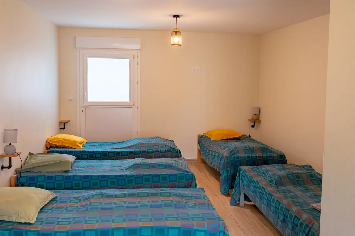 La chambre de six couchages du gîte de Malbouzon : six lits une place séparés, parquet clair et suspensions en verre