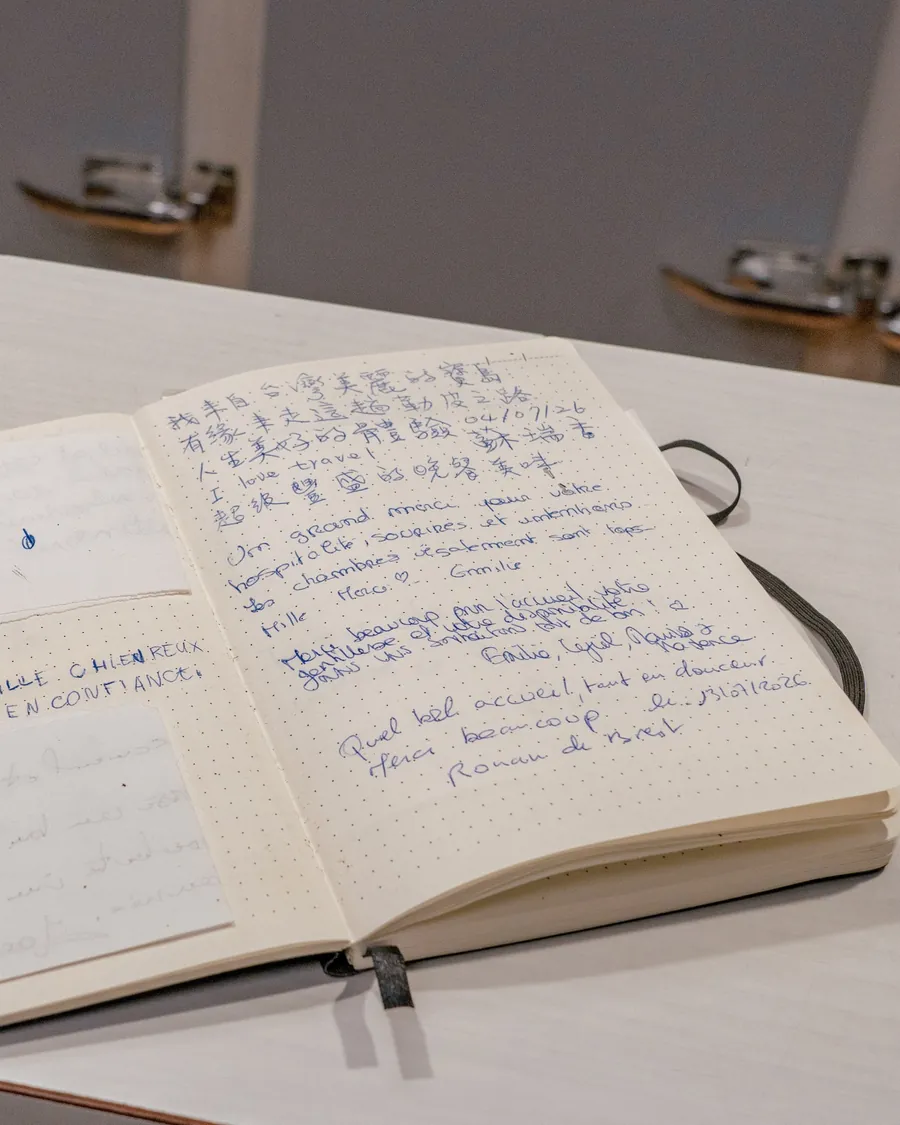 Le livre d'or du gîte ouvert sur une table : des pages manuscrites, dont un message laissé en caractères asiatiques