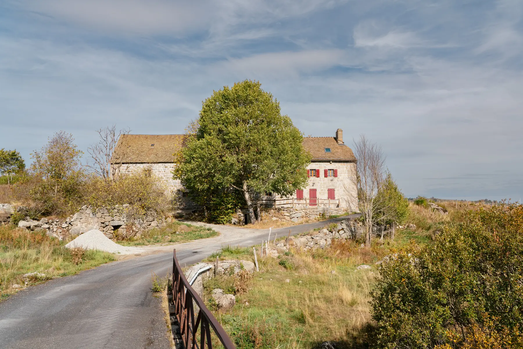 Le Moulin de la Folle : la bâtisse de granit sous son toit de lauzes, le petit pont et la route qui part vers Malbouzon — c'est ici qu'on quitte le GR 65