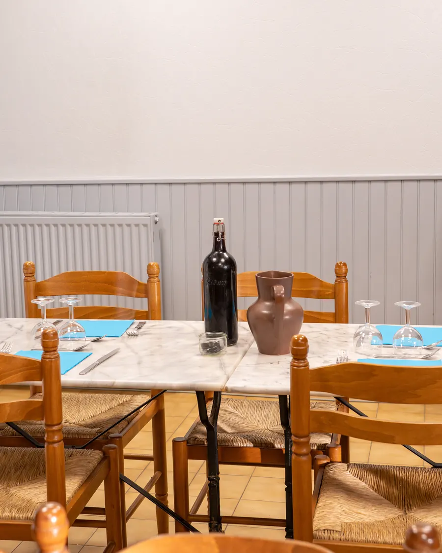 La grande table du gîte dressée pour le repas du soir : carafe, verres et chaises paillées
